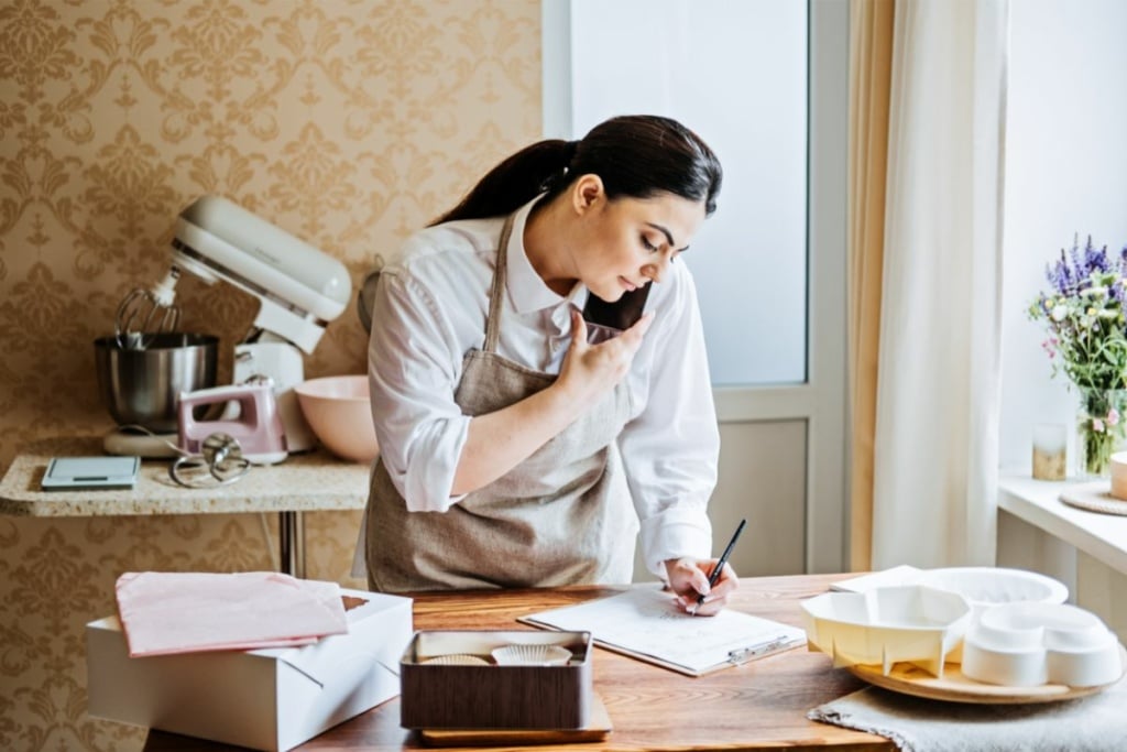 Femme avec un tablier, au téléphone et remplit des papiers.