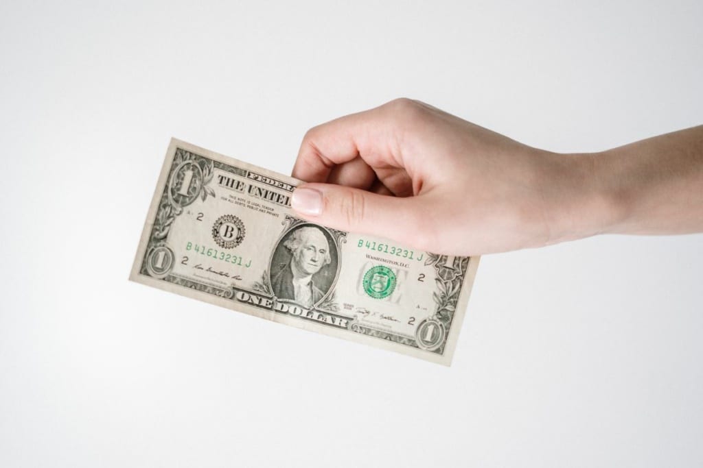 Une main tient un billet d'1 dollar.