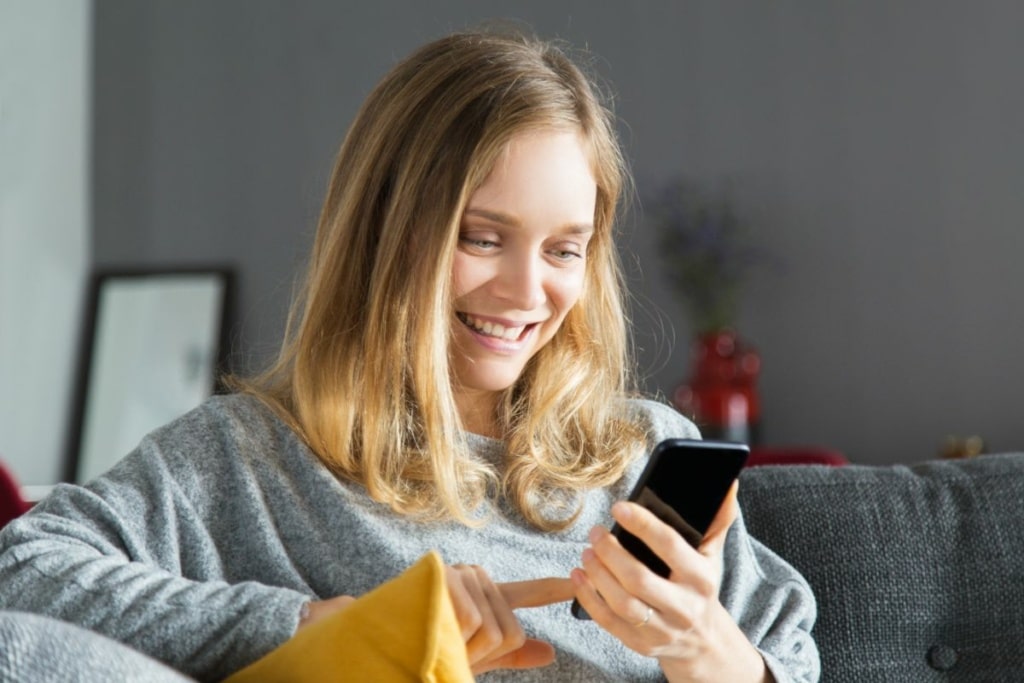 Une femme souriante utilise son smartphone.