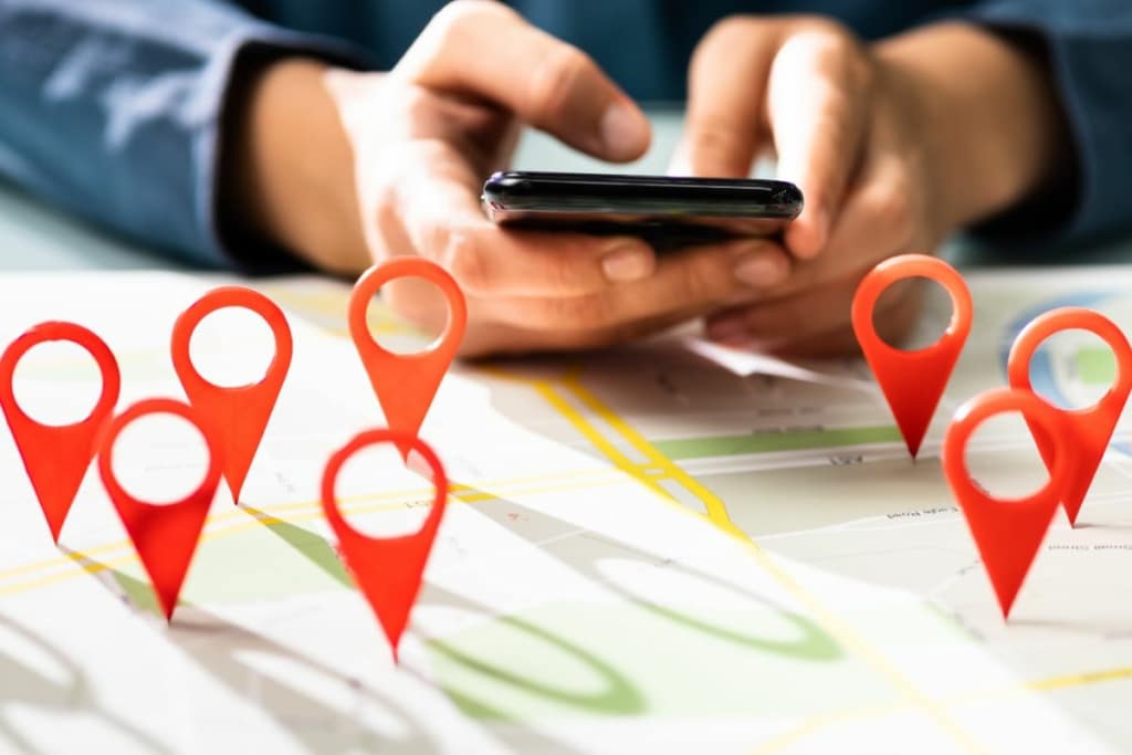 mains effectuant une recherche sur smartphone et pins sur une carte locale