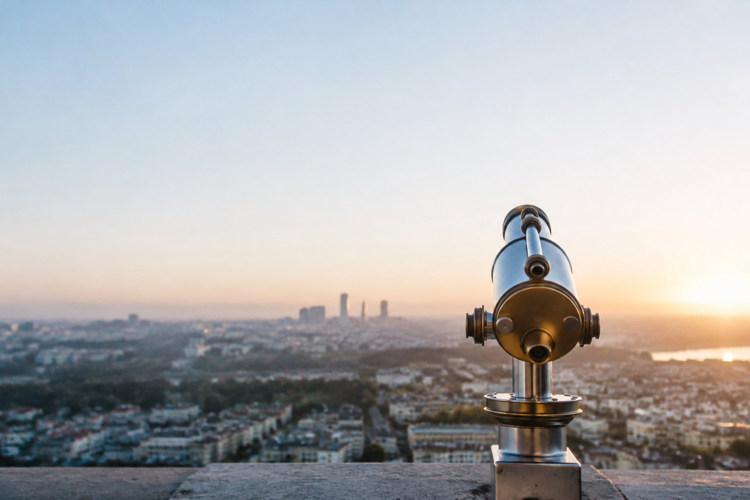 Une longue-vue métallique dirigée vers un panorama urbain au coucher du soleil.